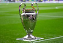كأس بطولة دوري أبطال أوروبا اللامع موضوع على قاعدة شفافة داخل أرضية الملعب الخضراء.