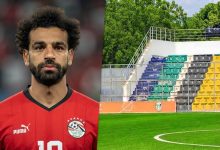 محمد صلاح بقميص منتخب مصر بجانب ملعب جوبا في جنوب السودان، مع ظهور أرضية العشب الصناعي ومدرجات الاستاد، في صورة رياضية تعبر عن غياب قائد الفراعنة عن مواجهة جنوب السودان بسبب طبيعة أرضية الملعب